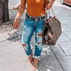 Person wearing distressed low waist jeans and holding a designer handbag.