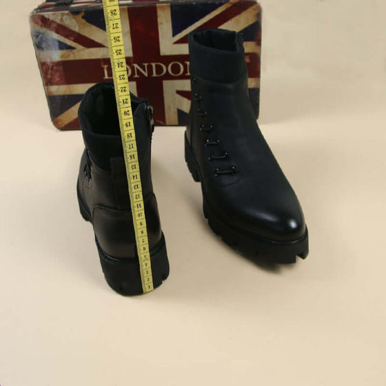 women's black ankle motorcycle boots with measuring tape on a vintage London-themed background.