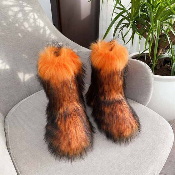 Women's closed toe plush snow boots in orange and black fur, placed on a chair with greenery in the background.