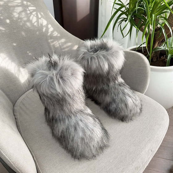 Women's closed toe warm fluffy plush snow boots in grey fur, resting on a cozy sofa with indoor plants.