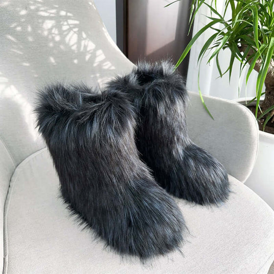 Women's closed toe plush snow boots in black faux fur, resting on a chair with natural light and greenery.