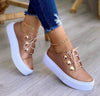 Lace-up flats sneakers with rivet detailing on a woman's feet.