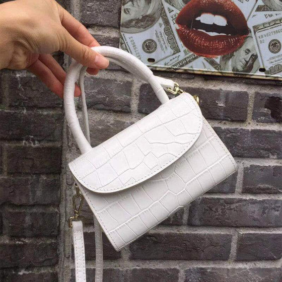 Luxury white leather handbag with textured design and hard handle against a brick wall background.