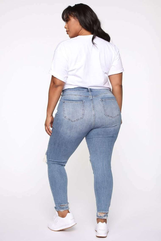 Plus size woman wearing stretch ripped jeans in light blue, rear view.