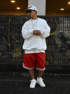 Men's solid color round neck long sleeve sweatshirt styled with red shorts, against urban background.